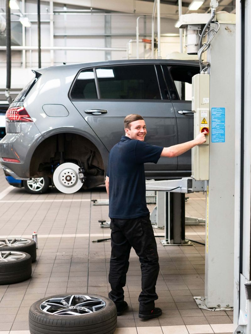 A technician working on a VW golf that's raised on a ramp with the wheel removed