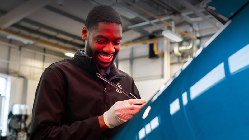 A technician inspecting a window wiper blade on a blue VW car