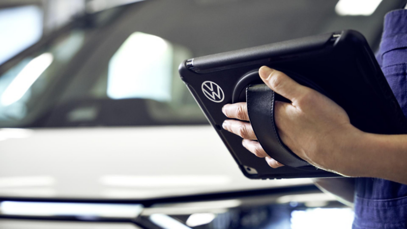 Mano sosteniendo tablet con logo de Volkswagen durante diagnóstico técnico. Servicio postventa oficial VW.