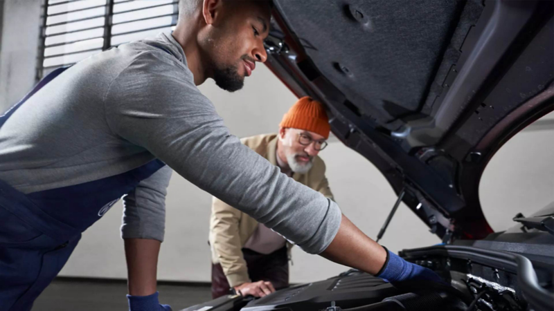 Técnico de Volkswagen revisa motor de camioneta SUV e indica a conductor de problemas. 