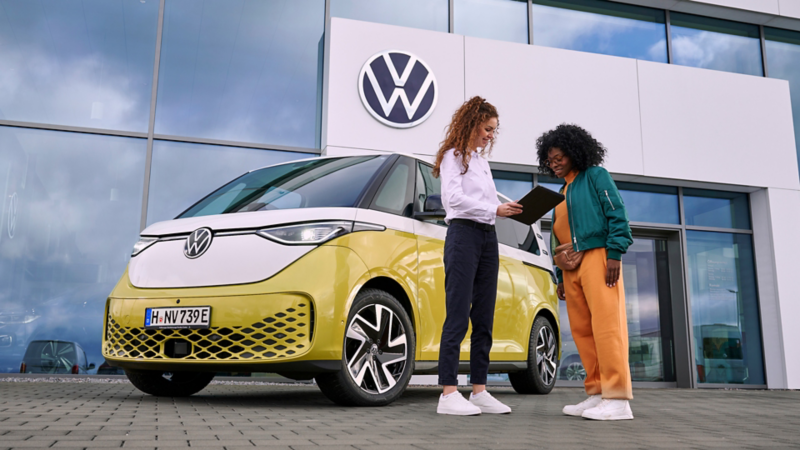 Una mujer del servicio técnico de VW hablando con una mujer, al lado del VW ID. Buzz.