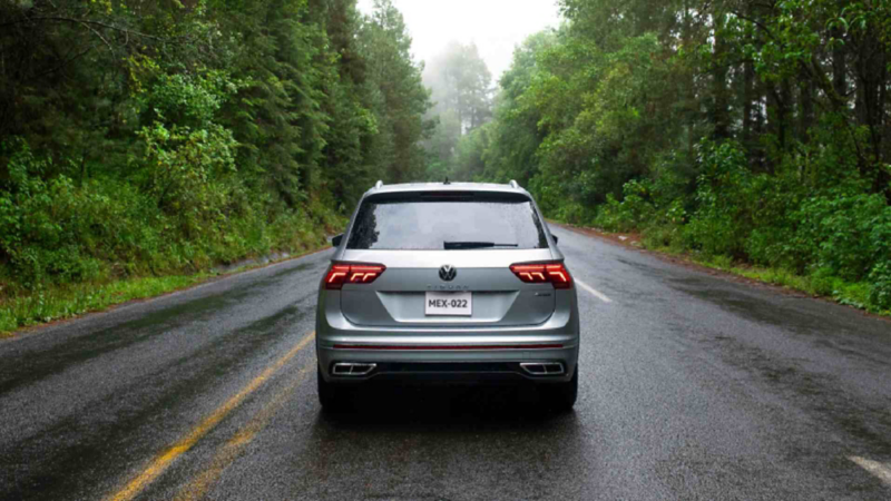 Tiguan 2023, versión R Line en color gris, avanza en una carretera boscosa. 