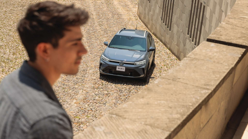 Volkswagen Nivus en color gris avanza sobre calle adoquinada con hombre desenfocado en primer plano.