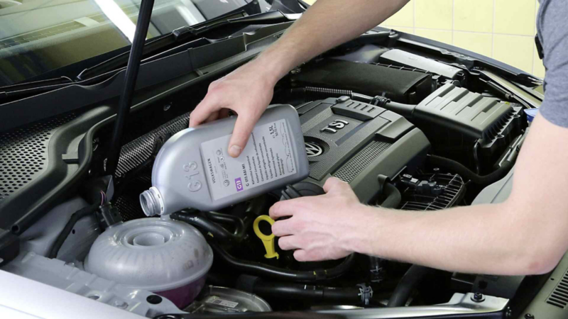Hombre vierte anticongelante en el depósito dentro del motor de un auto Volkswagen. 