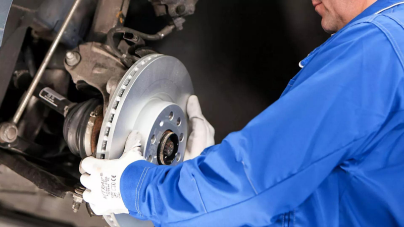 Técnico de Volkswagen toma disco de freno en taller de reparación. 