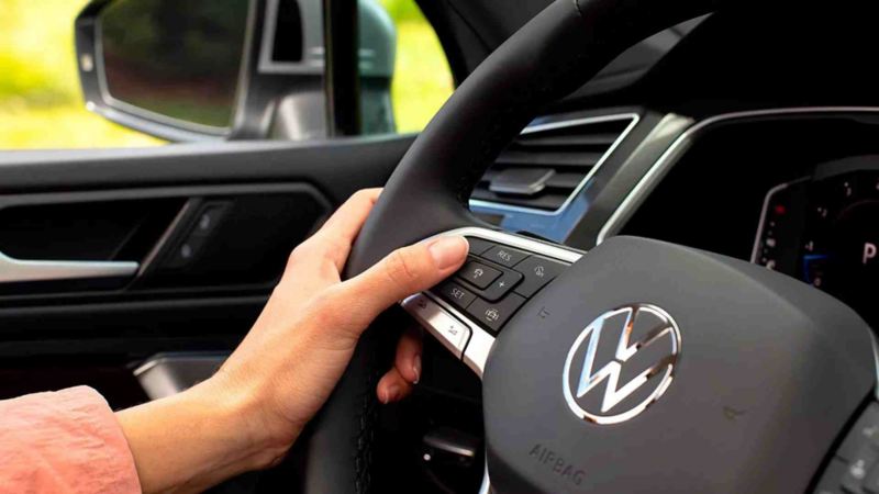 Mano de conductor toma el volante de un SUV de Volkswagen, con logo VW al centro.
