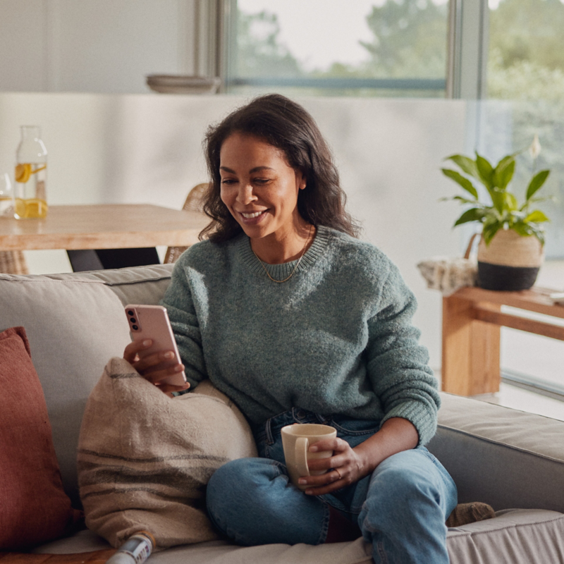 A woman lies on the sofa and looks at her smartphone