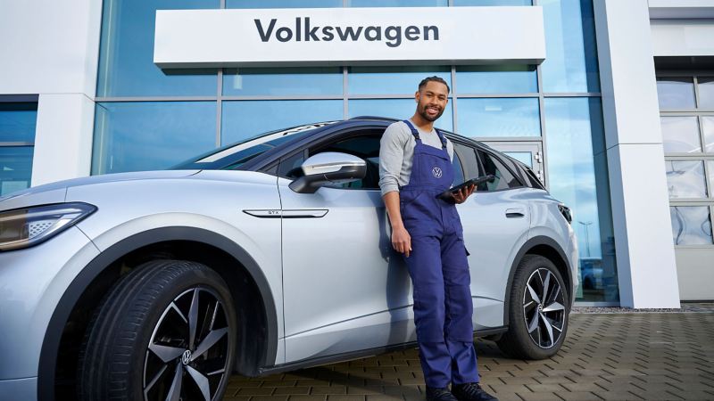 A VW engineer standing against a silver model holding an ipad