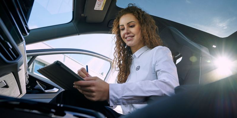 A service employee with a tablet in her hand sits in the passenger seat of a VW car