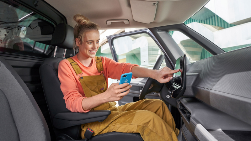 A woman using the touchscreen of the an VW ID. car and holding her mobile phone