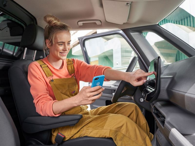 A woman using the touchscreen of the an VW ID. car and holding her mobile phone