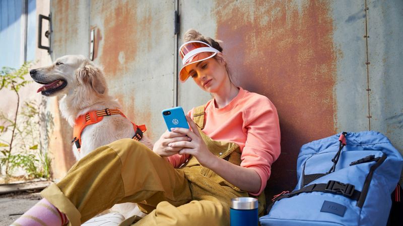 A young woman checks her smartphone for the latest ID. software updates, a dog sits next to her