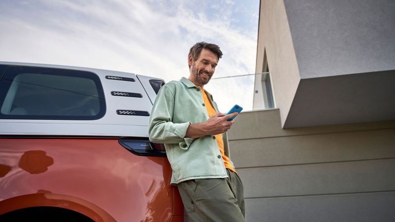 a man leaning against the back of a Volkswagen looking at his phone