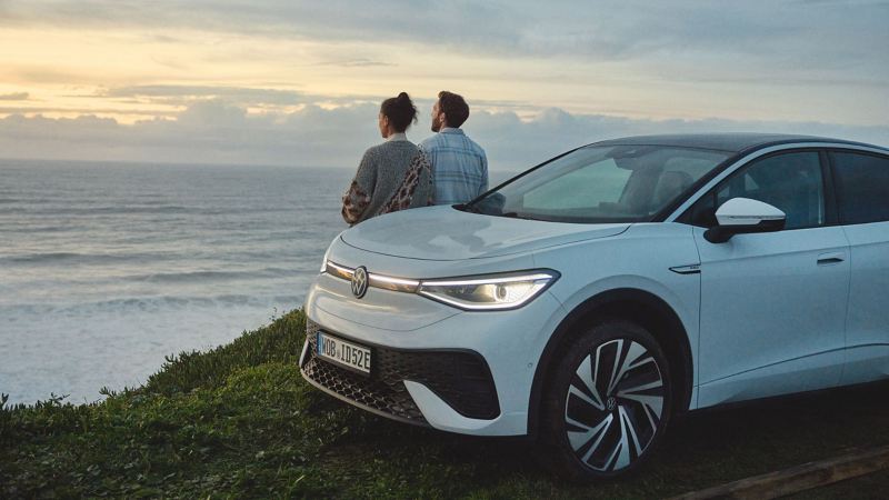 A VW ID. model parked on the coast with a couple looking out to sea