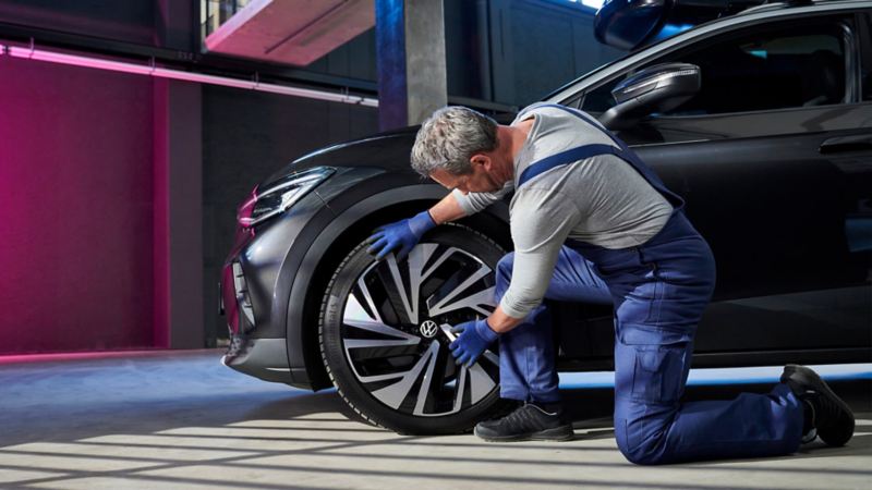 Un homme vêtu d'une salopette s'occupe de l'entretien d'un pneu avant côté conducteur d'une Volkswagen ID.4