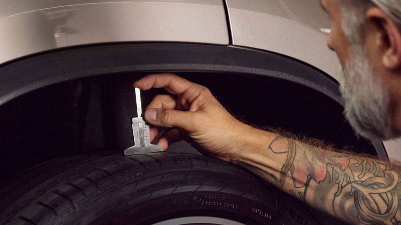 A Volkswagen service employee is measuring the tyre tread depth