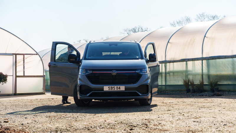 Volkswagen Transporter parked at a charging point outside a building while workers unload cargo.