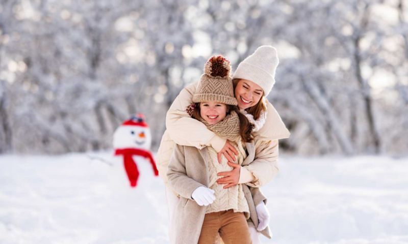 Ripresa di una madre mentre abbraccia la figlia e sorride insieme a lei in un parco ricoperto di neve. 