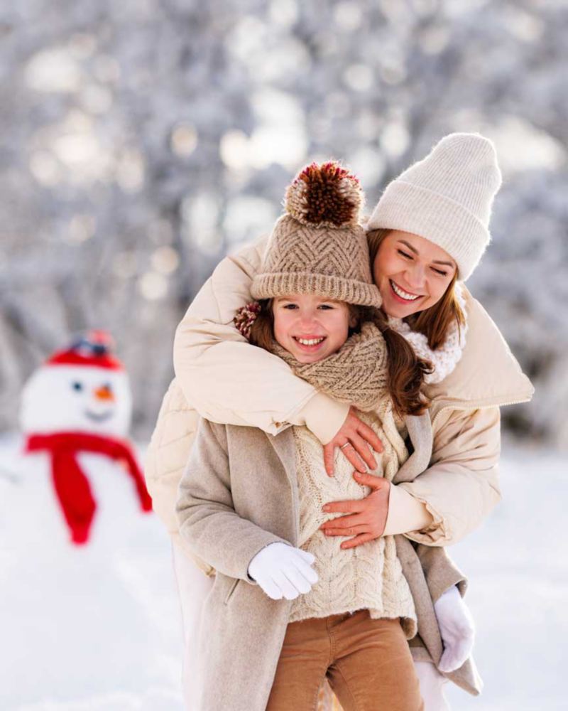 Ripresa di una madre mentre abbraccia la figlia e sorride insieme a lei in un parco ricoperto di neve. 