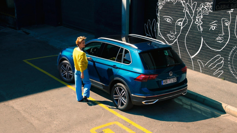 Tiguan bleue stationné, vue de 3/4 arrière. Une femme s'apprête à ouvrir la portière conducteur.