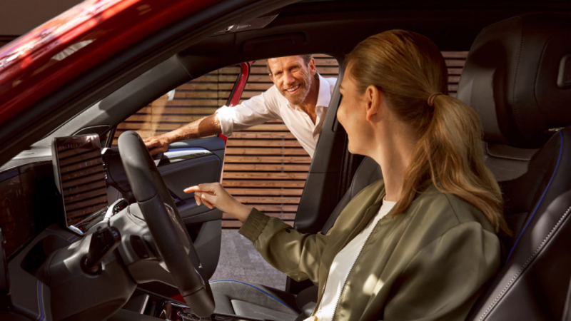 Una chica sentada en un Volkswagen hablando con un hombre parado fuera, Volkswagen nuevo en stock