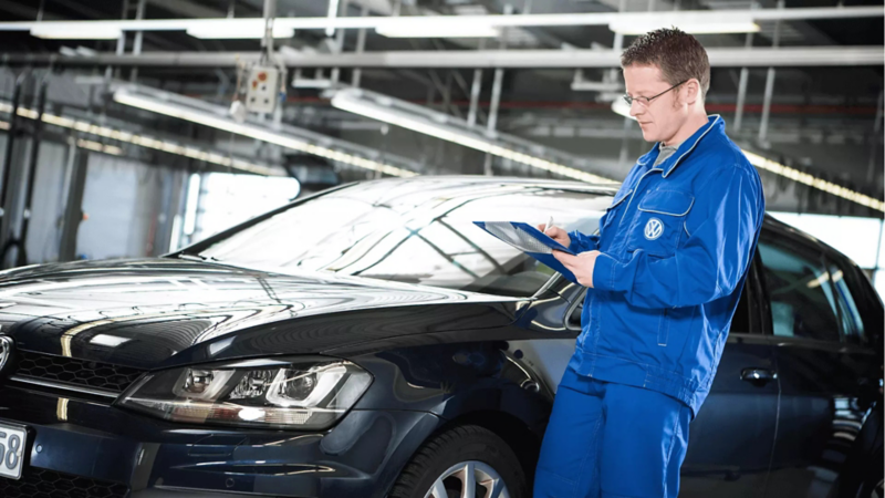 pracownik serwisu volkswagena zapisuje coś na liście kontrolnej, w tle czarny samochód