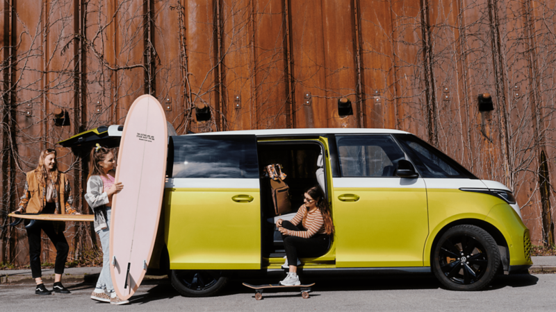 Tre kvinder står med surfboards ved en grøn og hvid id.buzz