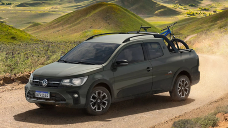 Camioneta Volkswagen Saveiro color verde en camino de tierra con bicicleta en la parte trasera, en un paisaje montañoso.