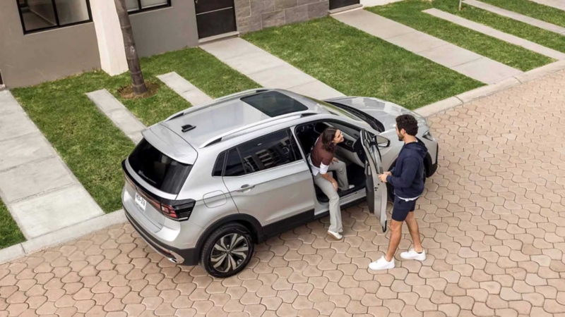 Volkswagen Taigun. Vista cenital de SUV de color plata con pareja bajando del auto en una residencia.
