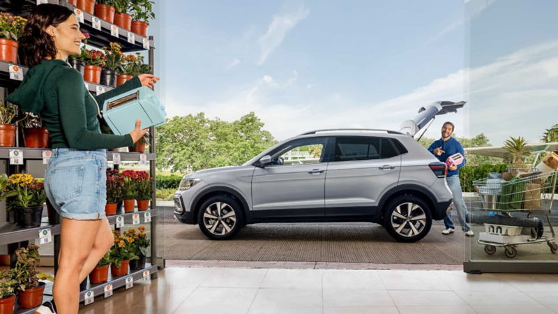 Mujer en tienda de jardinería y camioneta Taigun en color gris con cajuela abierta.