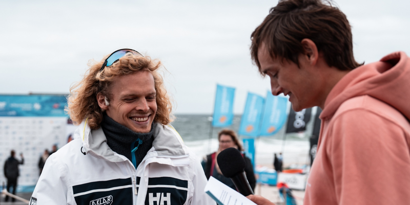 Im Rahmen einer Challenge befragt Niclas Nebelung am Strand einen Besucher des Windsurf World Cup Sylt.