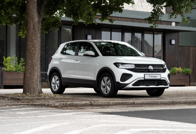 A man holds a happy boy in his arms in front of a blue VW T-Cross.