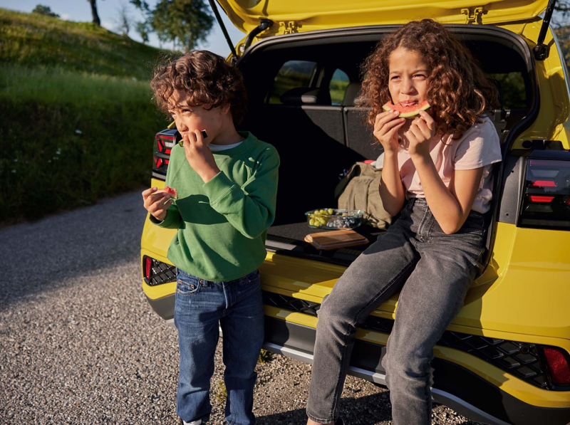 Two children sitting in the open boot of a yellow T-Cross