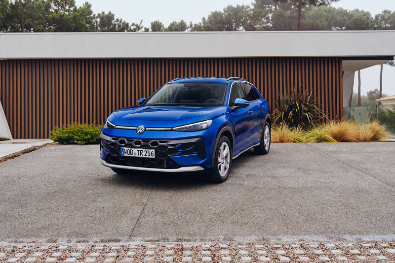 Front three-quarter view of a blue Volkswagen T-Roc SUV parked on a concrete driveway in front of a modern house.