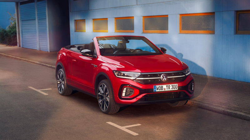 Volkswagen T-Roc Cabriolet rouge avec le toit ouvrant garé dans une rue devant un immeuble bleu