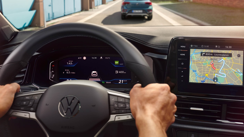 A close-up of a pair of hands on a steering and a multimedia display