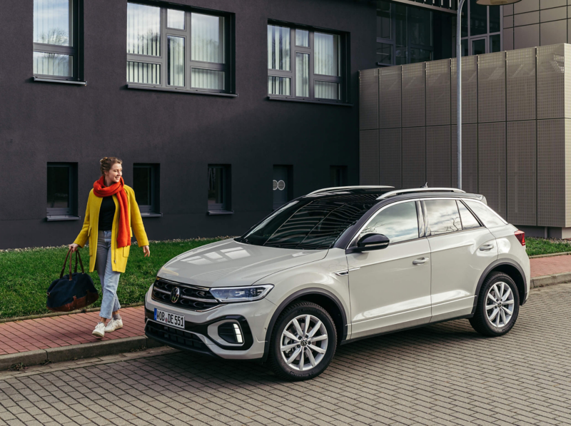 A woman walking away from a parked white VW T-Roc