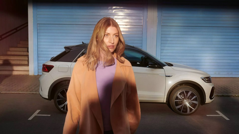 A woman walking away from a parked white VW T-Roc