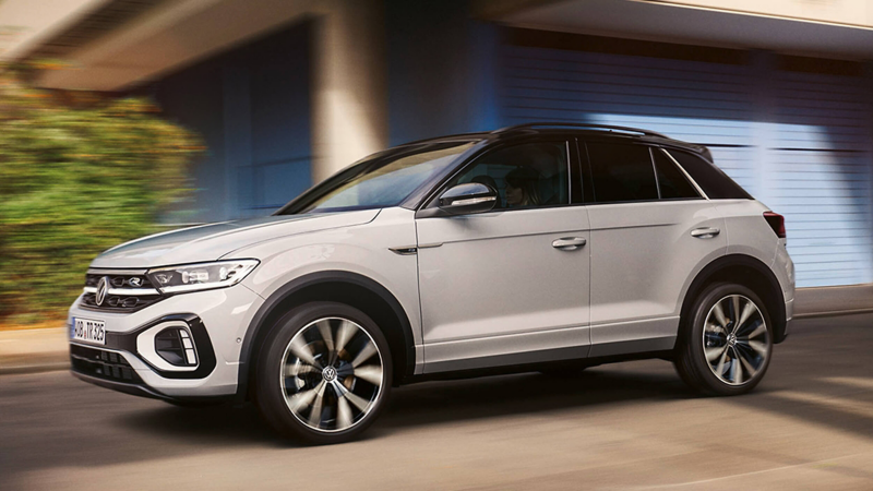 A side view of a white VW T-Roc driving past a building
