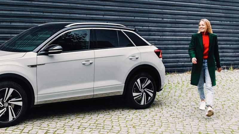 A woman walking away from a parked white VW T-Roc