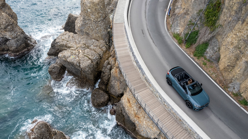 Da una vista dall'alto, si può vedere Carla Welti che guida la T-Roc Cabriolet su una strada costiera