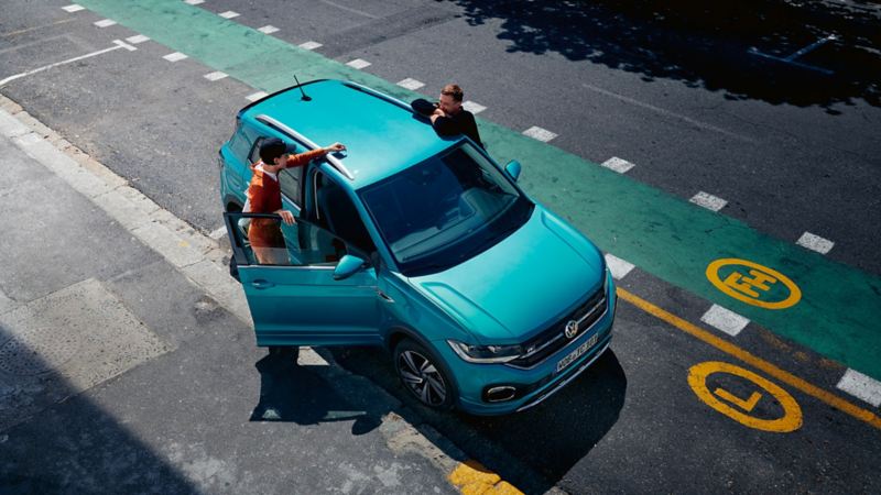 VW T-Cross bleu garé avec une porte ouverte et un couple qui discute de part et d'autre du véhicule