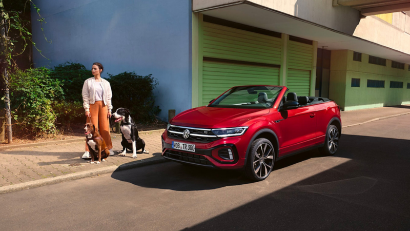 Une femme avec deux chiens debout à côté d'un VW T-Roc cabriolet rouge