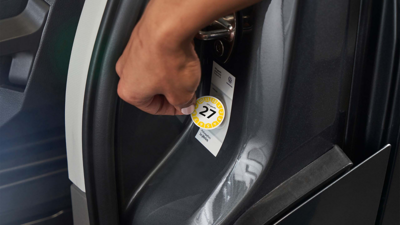 Ein UVV-Prüfsiegel wird an einem VW Fahrzeug angebracht.