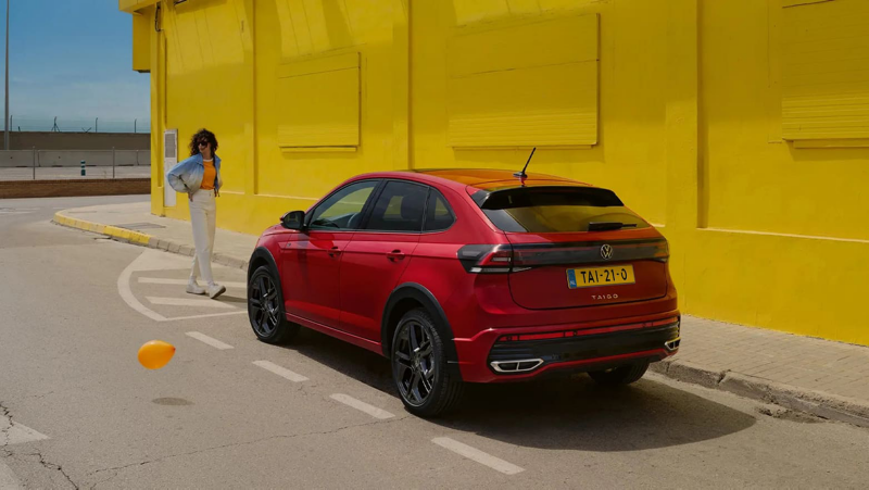 Rode Volkswagen Taigo staat geparkeerd, een vrouw staat voor de auto