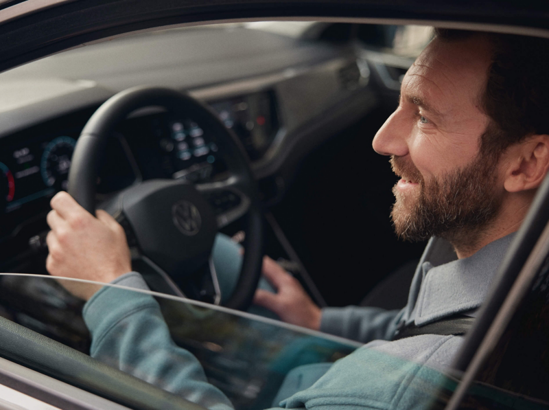A main sat in the cockpit of the VW Taigo holding the steering wheel with the car window halfway down.