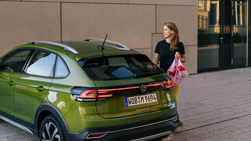 A woman shown exiting a VW Taigo parked in a city. 