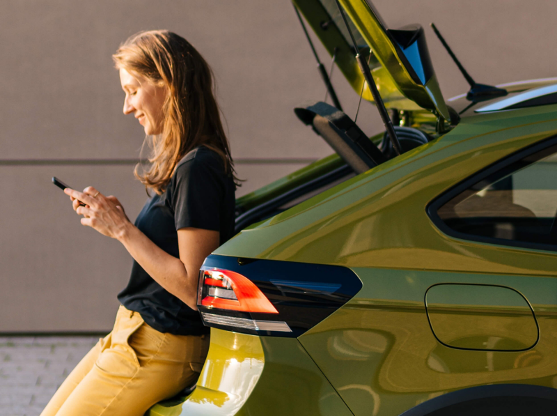 A woman leaning on the rear section of a VW Taigo while using her phone. 