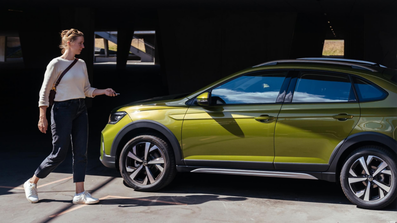 A woman walking toward a parked VW Taigo while unlocking it. 