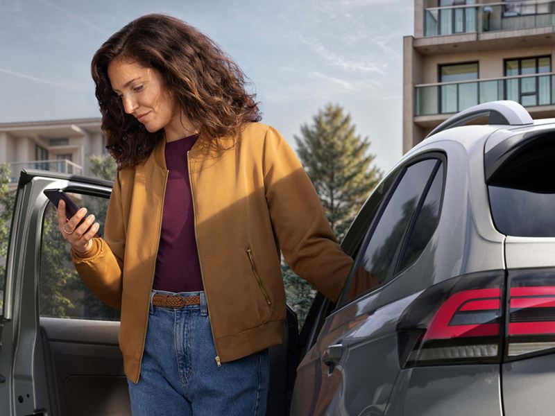 A woman holding a phone whilst standing by an opened car door